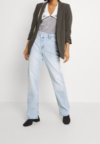 Lösa blå jeans med rak ben, kombinerade med en svartvit ginghamskjorta med vit krage, under en olivgrön kavaj.