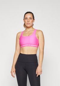 Rozā sporta krūšturis ar gludu, stiepjošu audumu un platu balto Under Armour logotipa joslu. Apvienots ar augsto vidukļa melno legingu.
