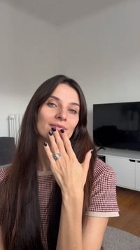 Modelka s dlhými tmavými vlasmi, oblečená v marónovom topu s vzorom, predvádza veľký strieborný prsteň na pravej ruke s čiernym lakom na nechtoch.