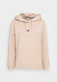 Sudadera beige con cordones, "Tommy Hilfiger Est. 1985" impreso en el pecho y pequeño logo de Tommy en el puño de la manga izquierda.
