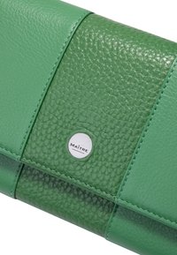 Portafoglio in pelle verde con pannelli texturizzati e lisci, impreziosito da cuciture a contrasto. Un logo in metallo è posizionato centralmente.