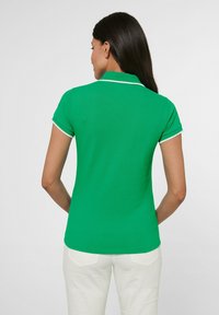 Groene polo met een slim fit, met een witte kraag en manchetten. De stof lijkt glad en iets gestructureerd.