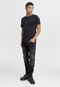 Zwarte katoenen t-shirt met korte mouwen, gedragen met zwarte slim-fit jeans en zwarte veterschoenen. Eenvoudig ontwerp zonder patronen of accenten.