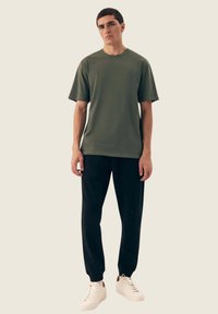 Oliwkowa koszulka bawełniana z krótkim rękawem, w połączeniu z czarnymi zwężanymi joggerami i białymi trampkami. Prosty design, bez widocznych wzorów czy logo.