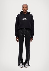 Black hooded sweatshirt with a white logo, paired with shiny black flared pants featuring slits, and silver shoes. Simple design, modern texture.