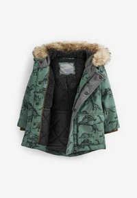 Veste matelassée verte avec motifs de dinosaures noirs, une bordure en fausse fourrure sur la capuche, et une doublure intérieure douce et texturée. Poches zippées incluses.