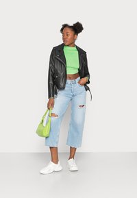 Jaqueta de motoqueiro de couro preto, top verde curto, jeans de perna larga azul claro com rasgos, tênis brancos e uma pequena bolsa verde.