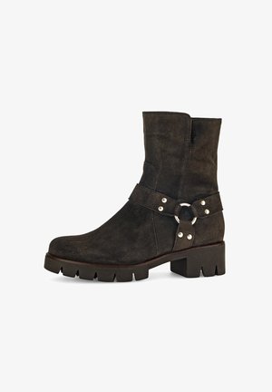 Bottines en cuir suédé marron foncé avec une semelle plate en caoutchouc, dotées d'une sangle avec des accessoires en métal argenté et d'un accent circulaire près de la cheville.