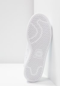 Baltas sporta apavi apakšda ar sešstūra rakstu, ar gludu virsmu un Adidas logotipu iespiestu papēdī.