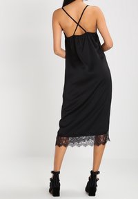 Musta satiini midi-mekko pitsireunalla, jossa on löysä malli, ristikkäiset spagettihihnat ja sileä koostumus.