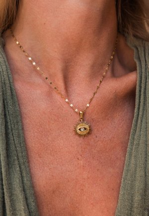 Gold chain necklace with an elongated, textured link design. Central pendant features a sunburst motif with a small gemstone at its center.