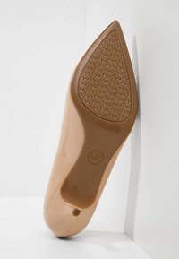 Chaussure à talon haut beige à bout pointu montrant la semelle avec un motif texturé du logo "MK" et la taille "7M" estampillée près du talon.