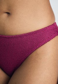 Fuksijos spalvos bikinių apačia, pagaminta iš tekstūruoto audinio, su aukštu kirpimu ir surinkimu ant juosmens, užtikrinančiu tvirtą prigludimą.