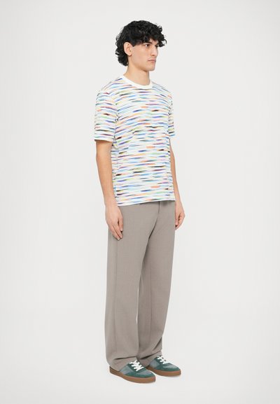 Večbarvna črtasta majica s kratkimi rokavi, združena s svetlo sivimi hlačami z gubami in zelenimi supergami z belimi poudarki.