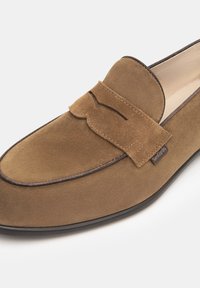 Braune Wildleder-Slipper mit einem schlanken Design, ausgestattet mit einer dekorativen Steppnaht, kontrastierendem Besatz und einem Markenetikett an der Seite.