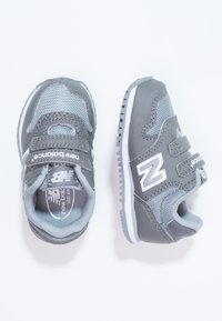 Szare dziecięce sneakersy z siateczkowego i syntetycznego materiału. Posiadają dwa paski na rzepy, białą podeszwę oraz wyraźne logo „N” po boku.