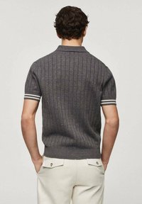 Polo gris à manches courtes avec une texture en relief verticale. Présente des poignets à rayures blanches et un ourlet droit. Porté avec un pantalon de couleur claire.