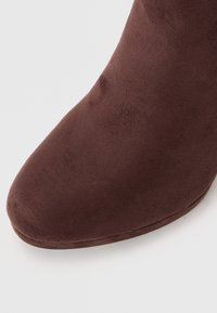 Brune semskete ankelstøvler med rund tå og glat tekstur. Sålen er let buet og har et strømlinet design uden synlige metaldele.