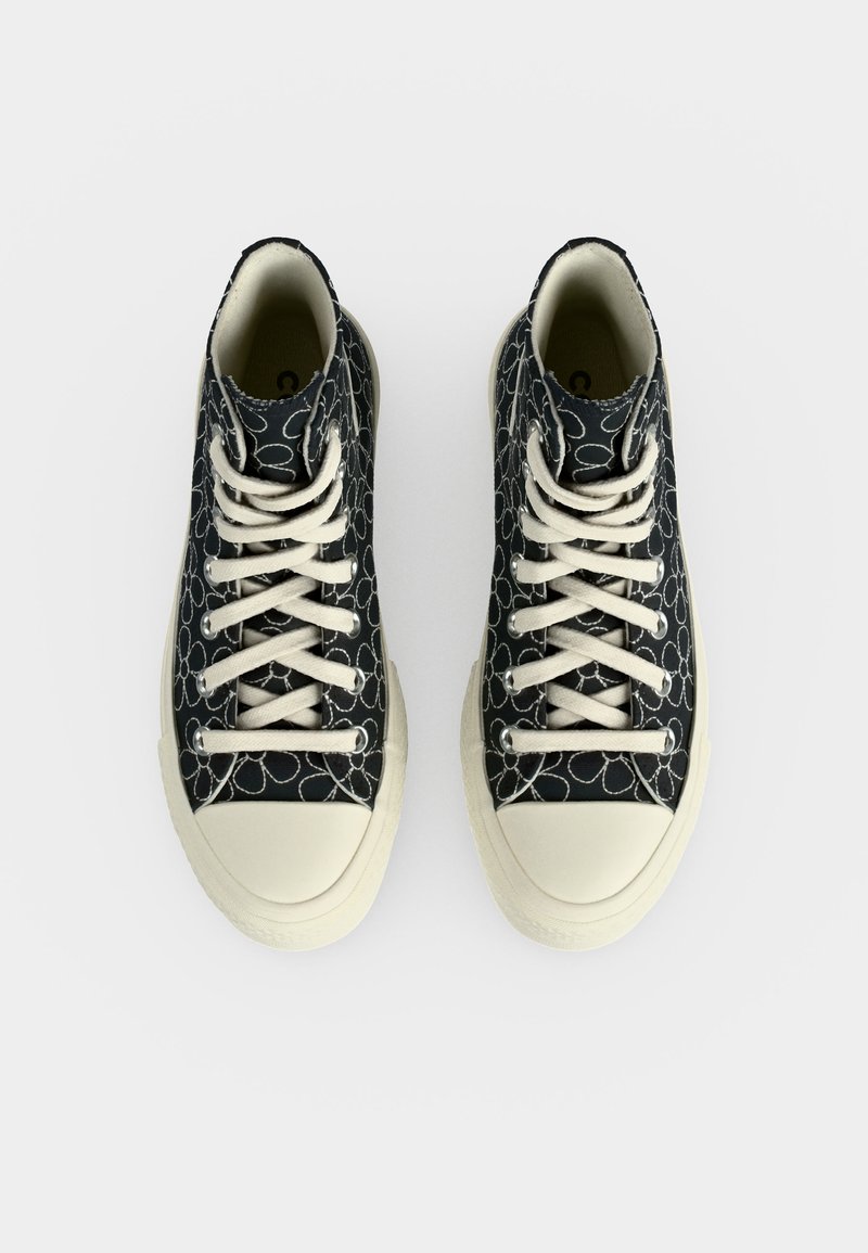Paar schwarze High-Top-Sneaker mit weißen floralen Umrissen, weißen Schnürsenkeln und cremefarbenen Gummi-Zehenschutzkappen und Sohlen, von oben betrachtet.