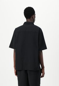 Camisa negra de manga corta con un ajuste relajado, cuello y una textura sutil. Presenta un dobladillo recto y un diseño minimalista.