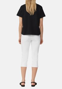Haut noir à manches courtes associé à un pantalon blanc court, présentant une coupe décontractée et une texture en coton lisse. Des sandales noires complètent le look.