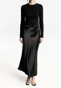 Top de punto negro de manga larga con detalles de tachuelas, acompañado de una falda maxi de satén negro lisos y sandalias de tacón con tiras.