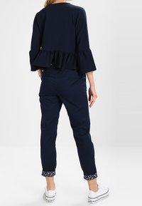 Marinblå kort topp med utsvängda ärmar och volangkant, kombinerad med marinblå byxor med blommönstrade manschetter och vita sneakers.