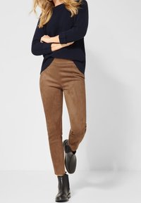 Bruna mockaskinnsbyxor med en mjuk textur, kombinerade med en marinblå ribbad tröja och slanka svarta ankelstövlar.