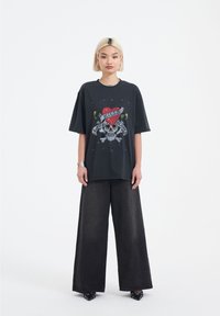 Černé grafické tričko s potiskem lebky a srdce, zkombinované s volnými tmavě šedými džíny. Modelka se nazdobila náušnicemi a stříbrným náhrdelníkem.