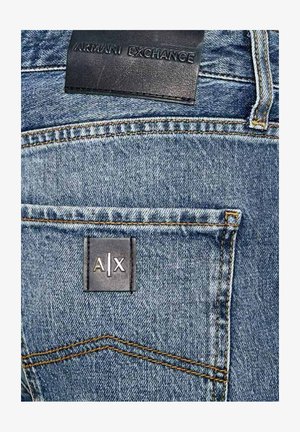 I jeans in denim blu chiaro presentano una targhetta in pelle scura con la scritta in rilievo "ARMANI EXCHANGE" e un'etichetta quadrata con "A|X" in argento.
