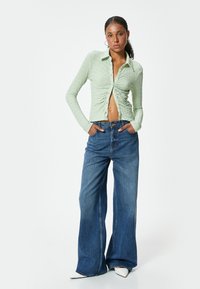 Lys grøn struktureret langærmet skjorte med krave, parret med løstsiddende blå denim flared jeans. Hvide spidse sko.