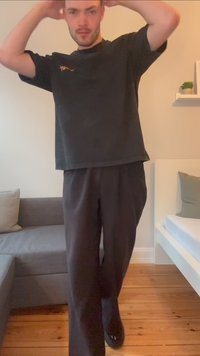 Camiseta preta oversized com mangas curtas apresenta um design bordado. Combinada com calças pretas largas e sapatos pretos, exibe um ajuste descontraído.
