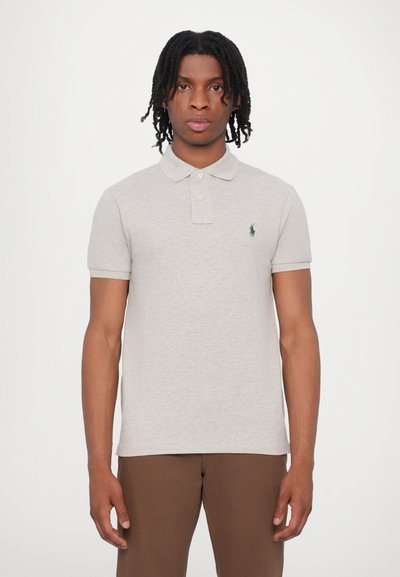 Polo gris hecho de algodón suave, con un cuello clásico, dos botones y un pequeño logo verde en el lado izquierdo del pecho. Mangas cortas.