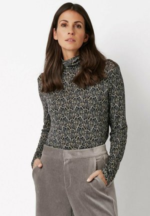 Long-sleeve, patterned turtleneck in dark shades with swirling designs; paired with light gray corduroy pants featuring side pockets.