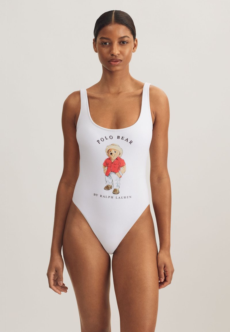 Vitt baddräkt i ett stycke med en färgglad björngrafik i röd tröja och texten "POLO BEAR BY RALPH LAUREN" under motivet.