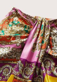 Tissu en soie présentant des motifs complexes aux couleurs vives : orange, turquoise, rose, violet et jaune, avec de riches accents dorés et une texture luxueuse.