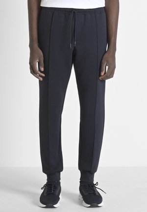 Pantalones jogger en color navy, hechos de tela suave, con cinturilla elástica, pliegues frontales y puños en los tobillos, combinados con zapatillas deportivas negras.