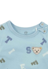 Světle modrá bavlněná košile s vyšívanou tváří medvěda a vícedílnými písmeny 'T', 'S', 'F', se zapínáním na patentky na rameni.