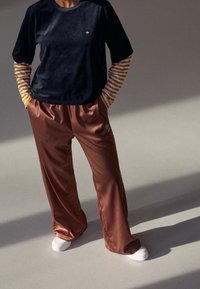 Marinblå sammetstopp med kort ärm ovanpå en randig långärmad tröja, parat med glänsande bruna sweatpants och vita sneakers.