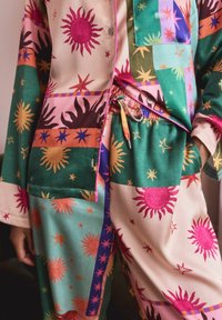 Buntes Pyjama-Set mit Sonnen- und Sternmustern in lebendigem Pink, Grün und Orange. Beinhaltet ein Oberteil mit Knöpfen und Hosen mit elastischem Bund.