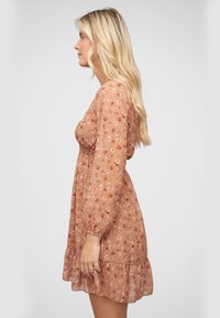 Robe fleurie en pêche avec de longues manches bouffantes et une taille froncée. Tissu transparent avec un ourlet froncé et de petits motifs floraux de différentes couleurs.