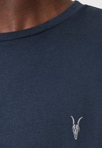 Námornícky bavlněný tričko s texturovaným povrchem a malým bílým vyšívaným logem kozí lebky na levém hrudním partii. Design s kulatým výstřihem.