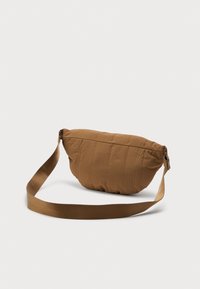 Καφέ μαλακή τσάντα χιαστί με ρυθμιζόμενο υφασμάτινο λουρί και διακριτή κάθετη ραφή σε απλό ανοιχτό φόντο.