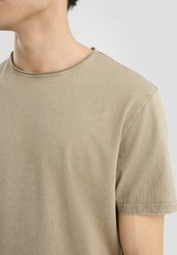 Beige bavlněné tričko s kulatým výstřihem, krátkými rukávy a jemnou, hladkou strukturou. Jemné švy kolem výstřihu.