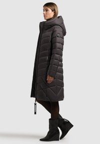 Čierny puffový kabát s diagonálnym prešívaním, kapucňou, predným zipsom a logom. Skombinovaný s čiernymi členkovými čižmami a pančuchami.