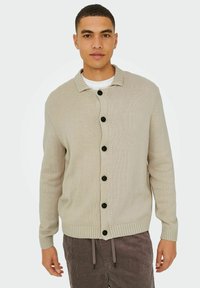 Beige strikket cardigan med skjortekrave, med seks sorte knapper foran og ribbede manchetter og forneden. Struktureret stof.