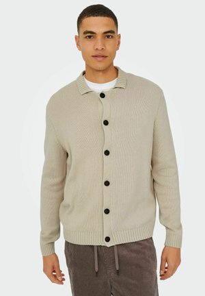 Beige gestrickte Strickjacke mit einem Hemdkragen, ausgestattet mit sechs schwarzen Knöpfen auf der Vorderseite sowie gerippten Bündchen und Saum. Strukturierter Stoff.