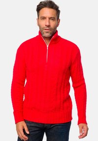 Roter Strickpullover mit einem Viertel-Reißverschluss, ausgestattet mit einem Kabelstrick-Muster und gerippten Bündchen und Saum. Getragen über dunklen Jeans.