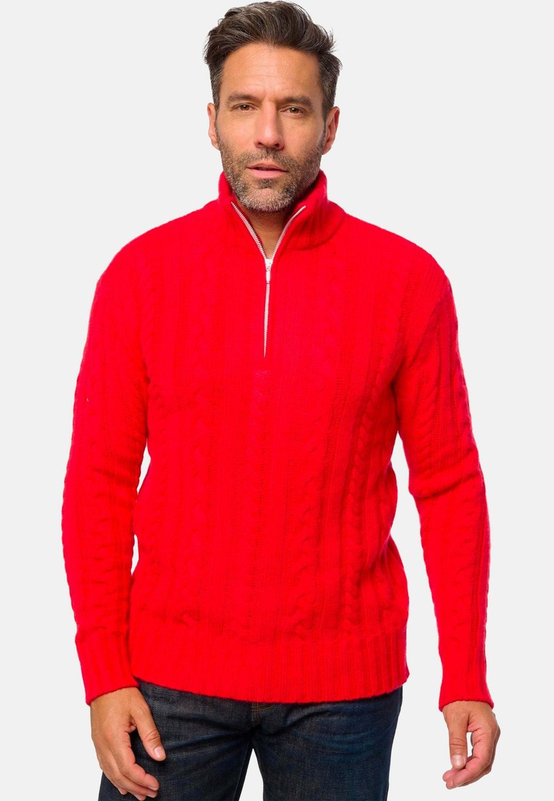 Roter Strickpullover mit einem Viertel-Reißverschluss, ausgestattet mit einem Kabelstrick-Muster und gerippten Bündchen und Saum. Getragen über dunklen Jeans.