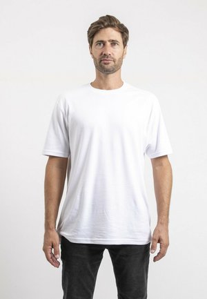 T-shirt blanc en coton à manches courtes, col rond et coupe décontractée. Porté avec un jean noir. Texture lisse, design minimal, sans motifs visibles.